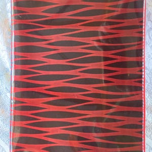 May include: A rectangular notebook cover with a red and black wave pattern. The design consists of red, curved lines on a black background. The edges are red, and the cover has a glossy finish, suggesting a protective layer.
