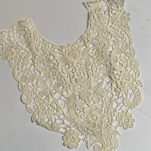 Pode incluir: Gola de renda marfim com um design floral e de rolagem. A gola é intrincadamente detalhada com padrões delicados e uma borda ondulada. Adequada para vários projetos de costura e artesanato.