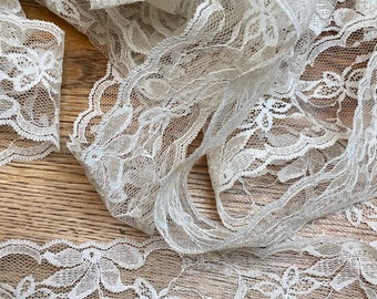 May include: White lace trim with a delicate floral pattern. The lace is soft and flowing, with a scalloped edge.