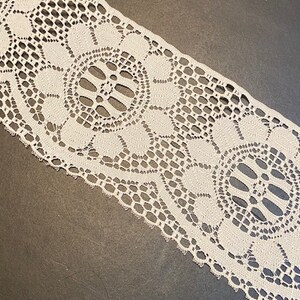 May include: White lace trim with a delicate floral pattern. The lace has a scalloped edge and is perfect for adding a touch of elegance to any project.