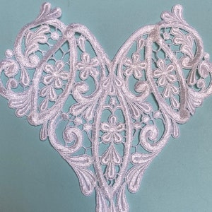 May include: White lace trim with a delicate floral pattern. The trim is shaped like a heart and has a scalloped edge.