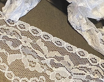 May include: White lace trim with a delicate floral pattern. The lace is soft and has a slightly ruffled edge.