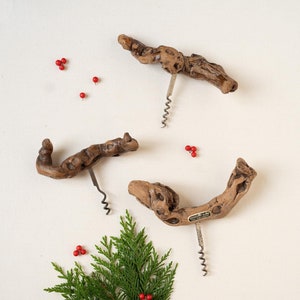 May include: Three wooden corkscrews with a rustic, natural look. The corkscrews are arranged on a white background with sprigs of greenery and red berries.