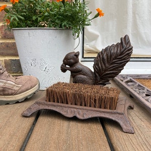 May include: A cast iron boot scraper with a squirrel design. The scraper has a brush and a base with a decorative design. The squirrel is holding a nut in its paws.