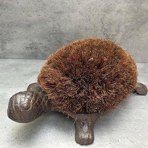 May include: A cast iron turtle boot scraper with a brown bristle brush on top. The turtle is a decorative design for a doormat.