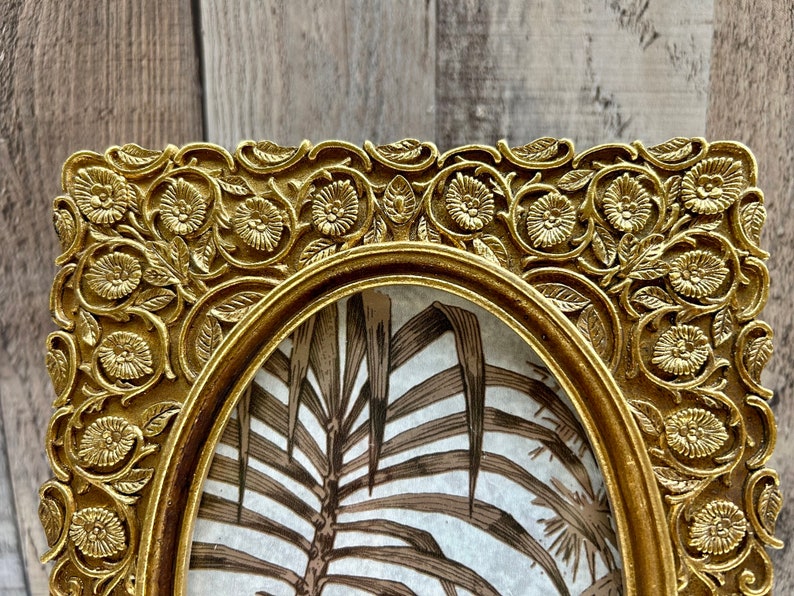 Peut inclure: Un cadre photo orn&eacute; de couleur or avec un motif floral d&eacute;taill&eacute;. Le cadre est de forme ovale et a un bord sur&eacute;lev&eacute;. Le cadre est vide et pr&ecirc;t &agrave; accueillir une photo.