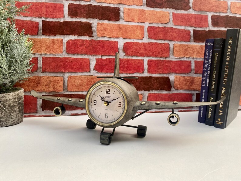 May include: A metal aeroplane clock with a brown and silver finish. The clock face is white with black numbers and hands. The aeroplane has a propeller and wings.