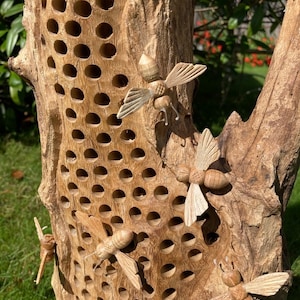 K&ouml;nnte beinhalten: Ein Bienenstock aus Holz mit einem Wabenmuster und geschnitzten Holzbienen, die an der Vorderseite befestigt sind. Der Bienenstock ist aus Naturholz gefertigt und hat ein rustikales Aussehen.