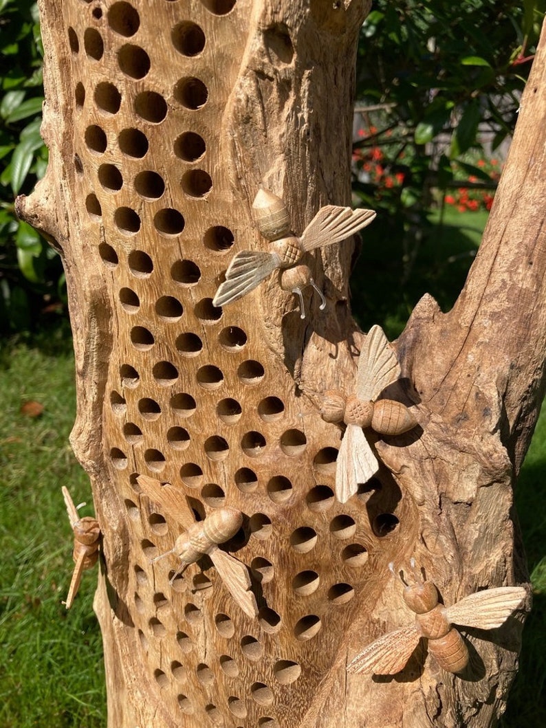 K&ouml;nnte beinhalten: Ein Bienenstock aus Holz mit einem Wabenmuster und geschnitzten Holzbienen, die an der Vorderseite befestigt sind. Der Bienenstock ist aus Naturholz gefertigt und hat ein rustikales Aussehen.