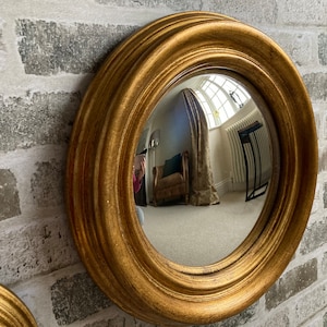 May include: A gold-framed round mirror with a convex lens. The mirror is hanging on a brick wall.