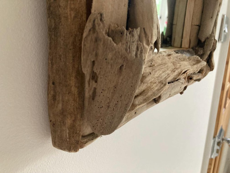May include: Close-up of a rustic wooden mirror frame made from driftwood. The frame is natural brown with a rough, textured surface.
