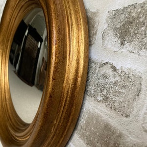 May include: A round mirror with a gold-colored frame. The frame has a decorative, fluted design.