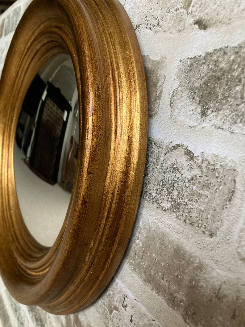 May include: A round mirror with a gold-colored frame. The frame has a decorative, fluted design.