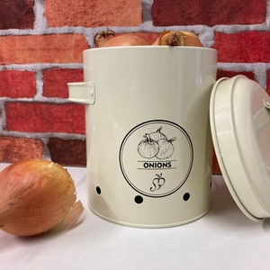May include: White metal onion storage container with a lid and holes for ventilation. The container has a black and white illustration of onions and the word "ONIONS" on the front.