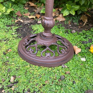 May include: A brown metal stand with a decorative heart-shaped design. The stand is sitting on a bed of green moss.