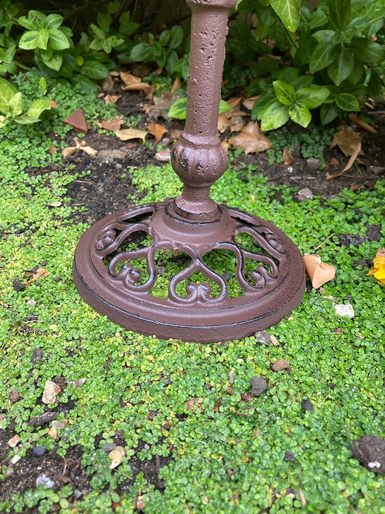 May include: A brown metal stand with a decorative heart-shaped design. The stand is sitting on a bed of green moss.
