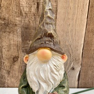 May include: A green and brown gnome figurine with a white beard and a pointed hat. The gnome is holding a fishing rod with a red bobber.