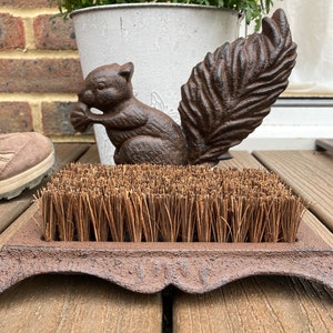 May include: A cast iron boot scraper with a brown coir brush and a squirrel design. The squirrel is holding a nut in its mouth and has a bushy tail.