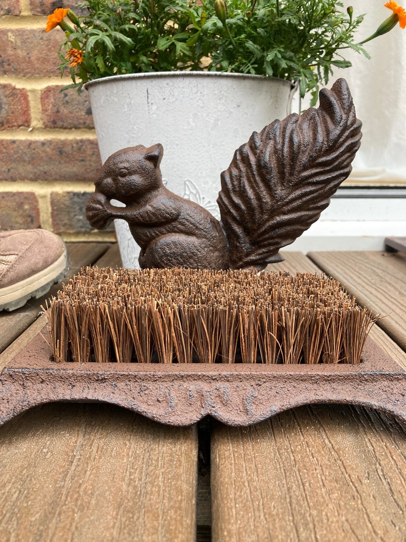 May include: A cast iron boot scraper with a brown coir brush and a squirrel design. The squirrel is holding a nut in its mouth and has a bushy tail.