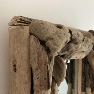 May include: A rustic mirror with a frame made of driftwood. The frame is thick and has a natural, weathered look. The mirror is rectangular and has a clear glass surface.