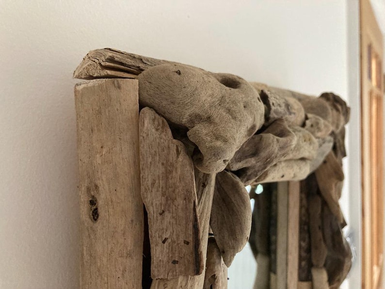 May include: A rustic mirror with a frame made of driftwood. The frame is thick and has a natural, weathered look. The mirror is rectangular and has a clear glass surface.