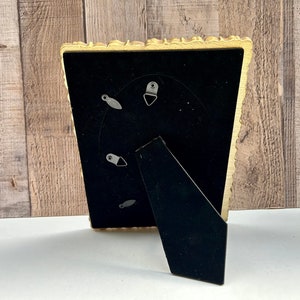 Peut inclure: Un cadre photo dor&eacute; avec un passe-partout noir et un bord festonn&eacute; d&eacute;coratif. Le cadre a un pied d'appui au dos.