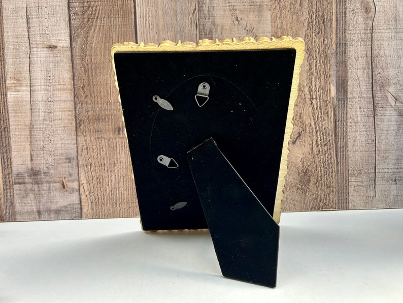 Peut inclure: Un cadre photo dor&eacute; avec un passe-partout noir et un bord festonn&eacute; d&eacute;coratif. Le cadre a un pied d'appui au dos.
