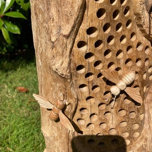 K&ouml;nnte beinhalten: Ein Bienenstock aus Holz mit einem geschnitzten Design aus Bienen und Waben. Der Bienenstock ist aus Naturholz gefertigt und hat einen rustikalen Look.