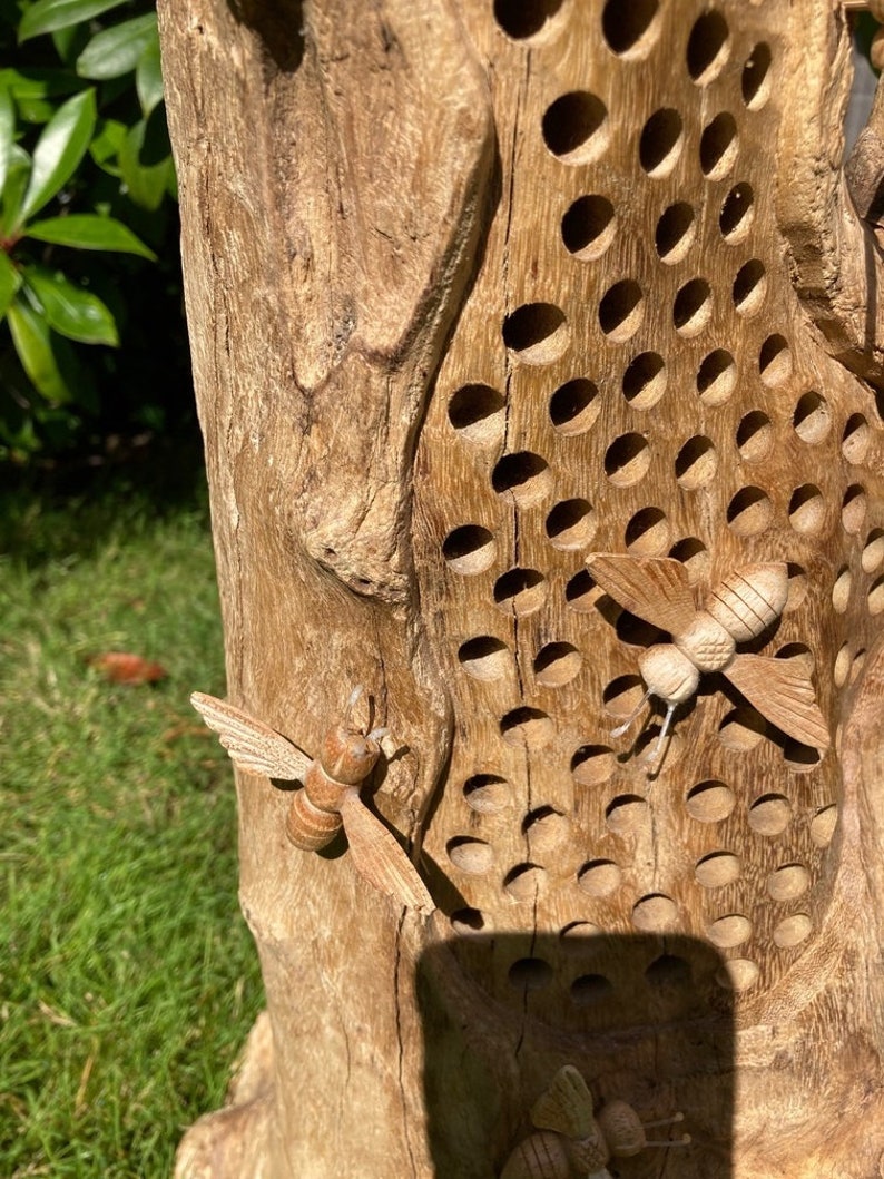 K&ouml;nnte beinhalten: Ein Bienenstock aus Holz mit einem geschnitzten Design aus Bienen und Waben. Der Bienenstock ist aus Naturholz gefertigt und hat einen rustikalen Look.