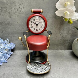 Peut inclure: Une horloge décorative en forme de fauteuil de barbier rouge et or. Le cadran de l'horloge est blanc avec des chiffres et des aiguilles noirs. Le fauteuil a un siège rouge et un repose-pieds. Un objet de décoration unique.