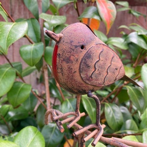 Peut inclure: Un piquet de jardin en métal en forme d'oiseau vieilli, avec une finition marron rouillé et des accents rouges. L'oiseau est perché sur une fine branche métallique, entouré de feuilles vertes. Ornement de jardin décoratif.