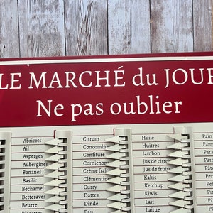Op de afbeelding: Een rood en wit bord met de tekst "LE MARCH&Eacute; du JOUR Ne pas oublier" in wit. Het bord bevat een lijst met voedingsmiddelen in het Frans, zoals "Abricots", "Citrons", "Huile" en "Pain".