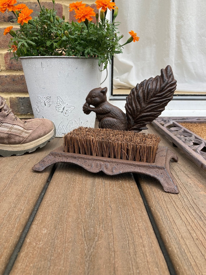 May include: A cast iron boot scraper with a squirrel design. The scraper has a brush and a base with a decorative design. The squirrel is holding a nut in its paws.