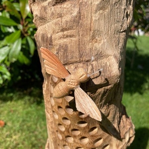 K&ouml;nnte beinhalten: Ein Bienenhotel aus Holz mit einer geschnitzten Holzbiene auf der Vorderseite. Das Bienenhotel hat viele L&ouml;cher, in denen Bienen nisten k&ouml;nnen.