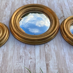 May include: Three round gold-framed mirrors of different sizes, reflecting a cloudy sky.