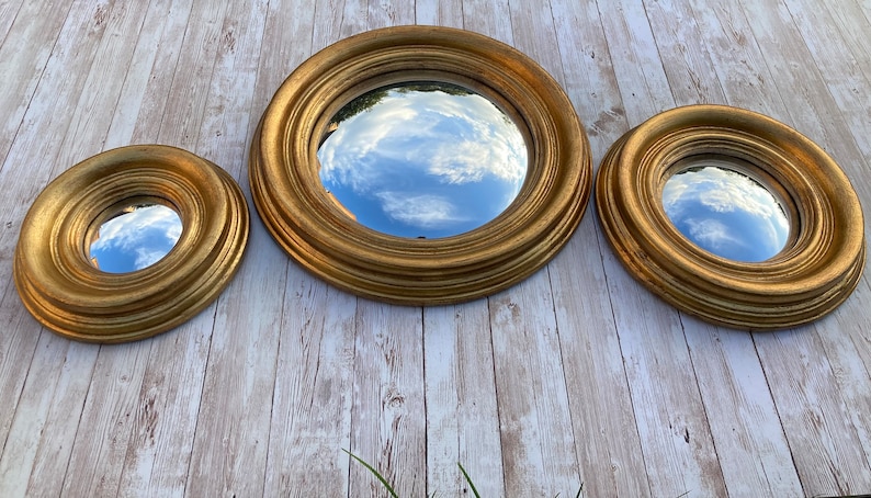 May include: Three round gold-framed mirrors of different sizes, reflecting a cloudy sky.