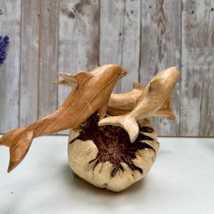 Peut inclure: Sculpture de dauphins en bois repr&eacute;sentant trois dauphins &eacute;mergeant d'une base textur&eacute;e et claire. Les dauphins sont sculpt&eacute;s dans du bois brun clair, avec des nageoires d&eacute;taill&eacute;es et des corps &eacute;lanc&eacute;s. Objet d&eacute;coratif.