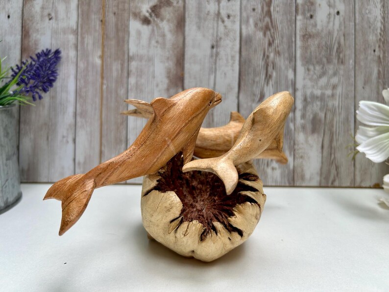 Peut inclure: Sculpture de dauphins en bois repr&eacute;sentant trois dauphins &eacute;mergeant d'une base textur&eacute;e et claire. Les dauphins sont sculpt&eacute;s dans du bois brun clair, avec des nageoires d&eacute;taill&eacute;es et des corps &eacute;lanc&eacute;s. Objet d&eacute;coratif.
