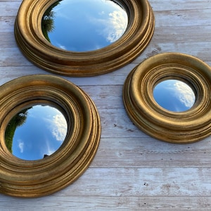 May include: Three round mirrors with gold frames of varying sizes. The mirrors reflect a blue sky with white clouds.