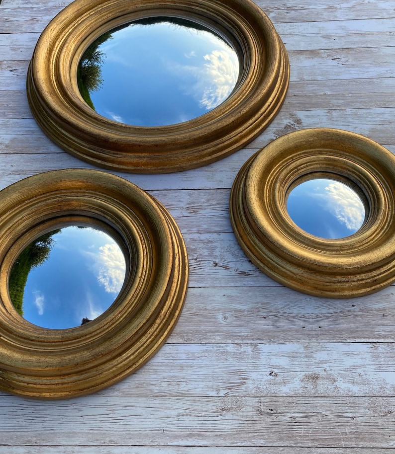 May include: Three round mirrors with gold frames of varying sizes. The mirrors reflect a blue sky with white clouds.