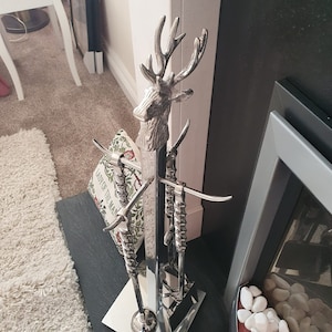 May include: Silver fireplace tool set featuring a deer head design. The tools include a poker, tongs, and a shovel. The set is mounted on a stand with a black base.