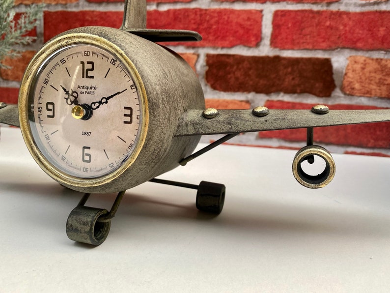 May include: A grey metal aeroplane clock with gold accents. The clock face has Roman numerals and the text "Antiquit&eacute; de PARIS 1887".