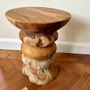 Peut inclure: Tabouret en bois artisanal avec une finition naturelle. Le tabouret présente un dessus rond et une base empilée composée de quatre sections de forme organique. Le grain et les variations de couleur du bois créent une esthétique rustique unique. Le tabouret mesure environ 46 cm de haut.