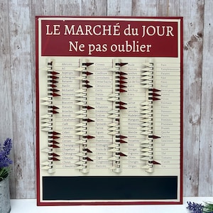 Op de afbeelding: Een rood en wit vintage-stijl boodschappenlijstbord met een schoolbordpaneel. Het bord heeft een lijst met Franse woorden voor voedingsmiddelen, zoals "citroenen", "ham" en "appels". De tekst "LE MARCH&Eacute; du JOUR" en "Ne pas oublier" staat op het bord gedrukt.
