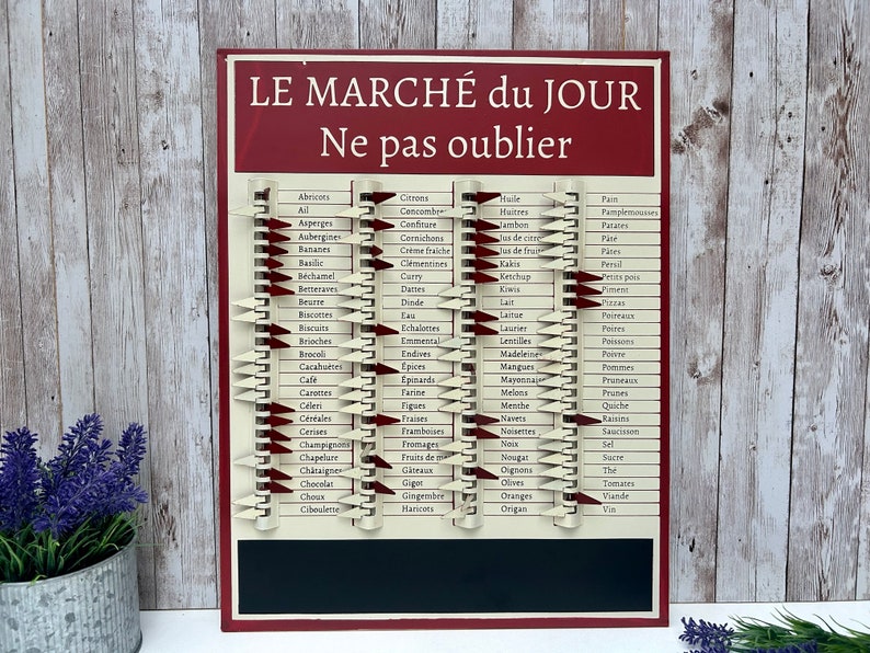Op de afbeelding: Een rood en wit vintage-stijl boodschappenlijstbord met een schoolbordpaneel. Het bord heeft een lijst met Franse woorden voor voedingsmiddelen, zoals "citroenen", "ham" en "appels". De tekst "LE MARCH&Eacute; du JOUR" en "Ne pas oublier" staat op het bord gedrukt.