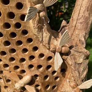 K&ouml;nnte beinhalten: Ein Bienenhaus aus Holz mit einem Wabenmuster und geschnitzten Bienen aus Holz. Die Bienen befinden sich in verschiedenen Positionen, einige fliegen und andere ruhen auf dem Haus. Das Haus ist aus Naturholz gefertigt und hat einen rustikalen Look.