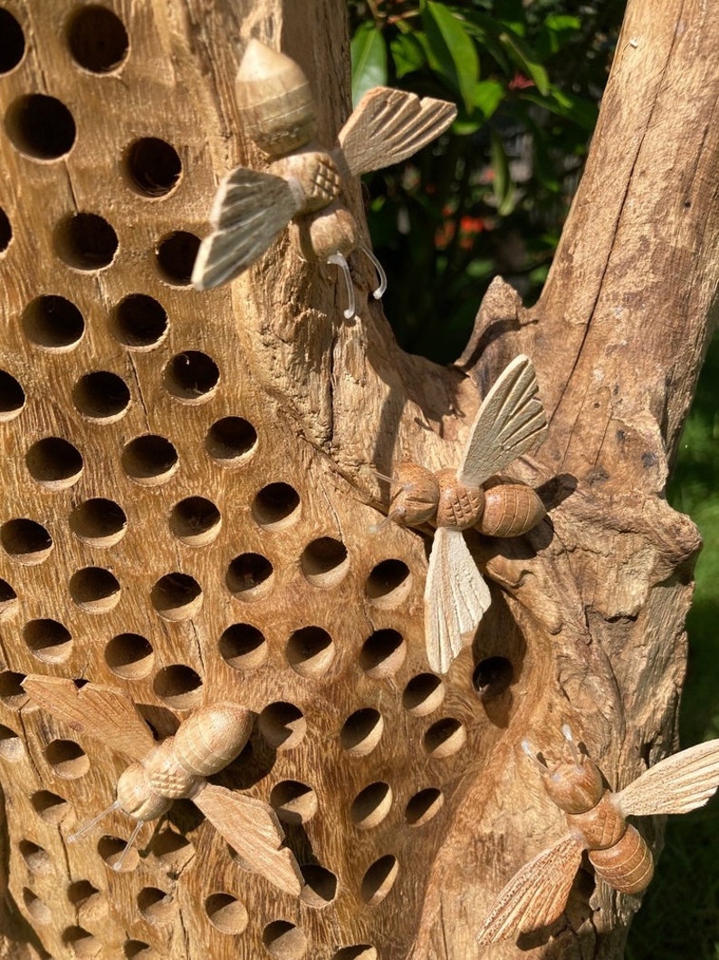 K&ouml;nnte beinhalten: Ein Bienenhaus aus Holz mit einem Wabenmuster und geschnitzten Bienen aus Holz. Die Bienen befinden sich in verschiedenen Positionen, einige fliegen und andere ruhen auf dem Haus. Das Haus ist aus Naturholz gefertigt und hat einen rustikalen Look.