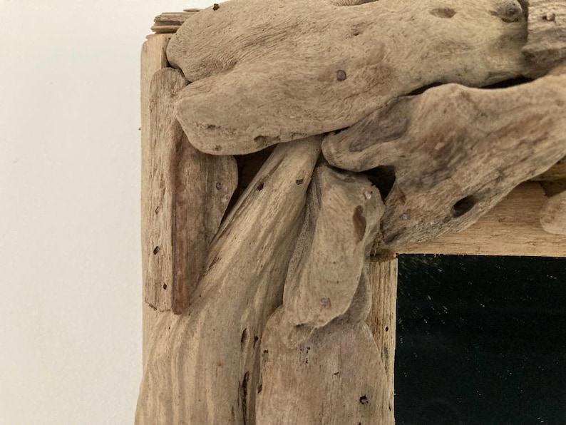 May include: A rustic mirror frame made from driftwood. The frame is made of natural wood with a rough texture and a dark brown color. The mirror is rectangular and has a black surface.