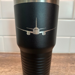 May include: Black stainless steel travel mug with a silver lid and an engraved airplane silhouette.