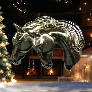 May include: A silver-colored sculpture of two horses' heads, with their necks intertwined, against a backdrop of a fireplace and a Christmas tree.